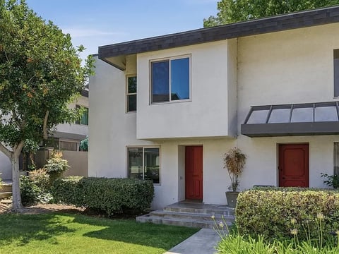 Modern white two-story house with red doors, blue windows, landscaped yard with green hedges and trees