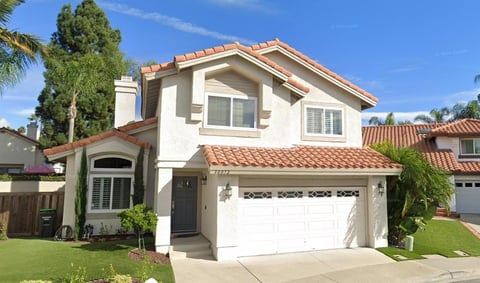 Two-story white house with terracotta tile roof, two-car garage, and well-maintained lawn under clear blue sky